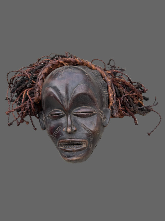 Carved wooden mask with braided hair on a light gray background